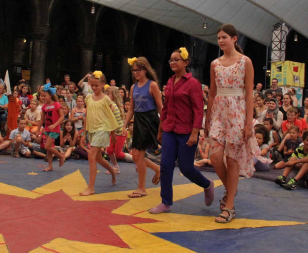 Mehrere Mädchen laufen barfuß oder mit Sandalen über eine Bühne vor einem Publikum.