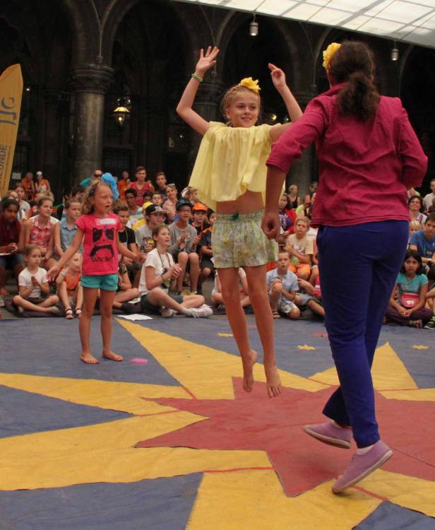 Ein Mädchen springt barfuß auf einer Bühne vor einem Publikum.
