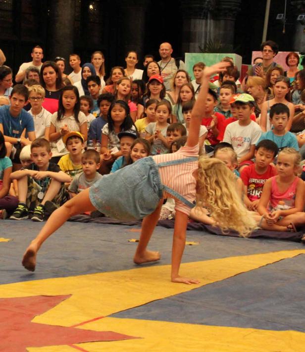 Ein junges Mädchen macht vor einem Publikum einen Handstand auf einer Bühne.