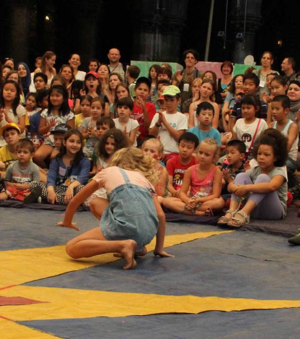 Ein Mädchen führt vor einer Gruppe von Kindern eine Akrobatikübung vor.