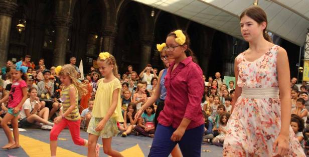 Eine Gruppe junger Mädchen läuft bei einer Modenschau vor einem Publikum.