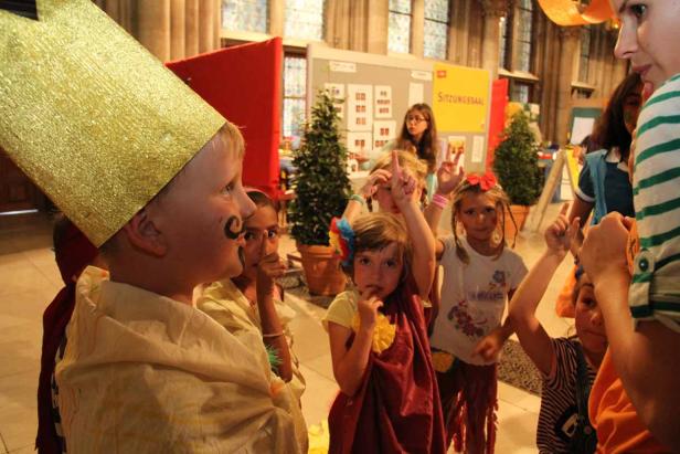 Eine Gruppe Kinder, einige mit Kostümen und Schminke, posieren in einem Raum.
