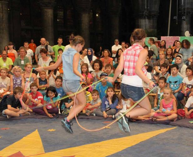 Zwei Mädchen springen Seil vor einer Gruppe von Kindern und Erwachsenen.