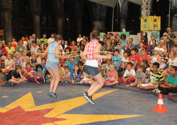 Zwei Mädchen springen Gummitwist vor einer Gruppe von Kindern und Erwachsenen.