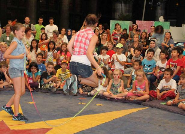 Ein Mädchen springt Seil vor einer Gruppe von Kindern und Erwachsenen.