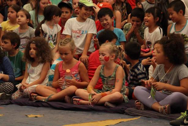 Eine Gruppe von Kindern sitzt auf dem Boden und schaut aufmerksam zu.