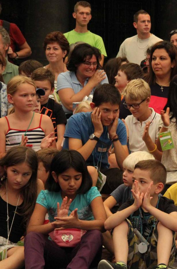 Eine Gruppe von Kindern und Erwachsenen sitzt und klatscht in die Hände.