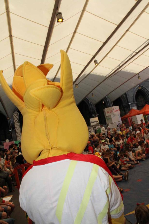 Ein gelbes Maskottchen steht vor einer Gruppe von Kindern.