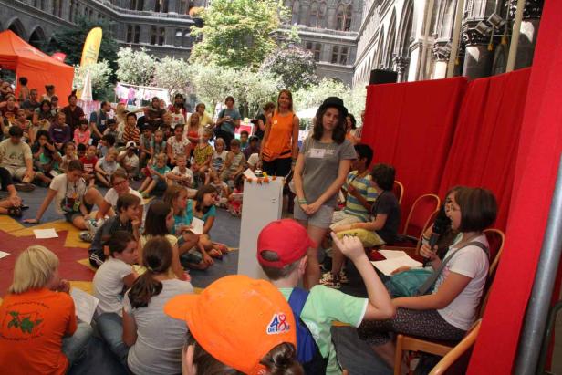 Eine Gruppe von Kindern sitzt auf dem Boden und hört einer Präsentation zu.