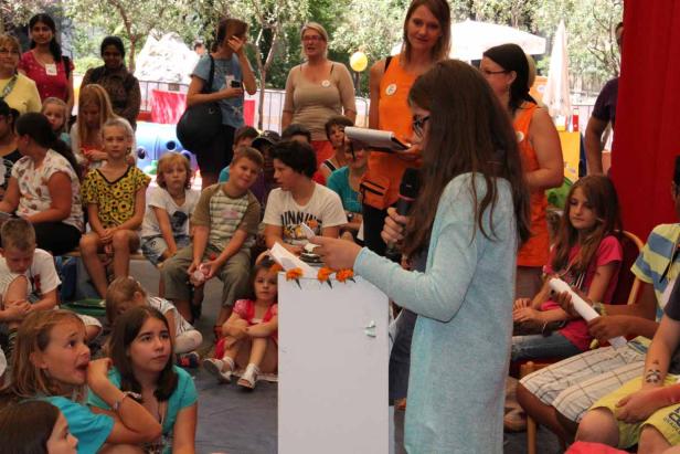 Ein Mädchen hält eine Rede vor einer Gruppe von Kindern und Erwachsenen.