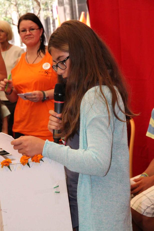 Ein junges Mädchen liest mit einem Mikrofon in der Hand von einem Blatt Papier vor.