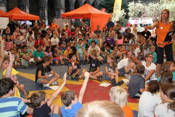 Eine Gruppe Kinder sitzt auf dem Boden, während eine Frau spricht.