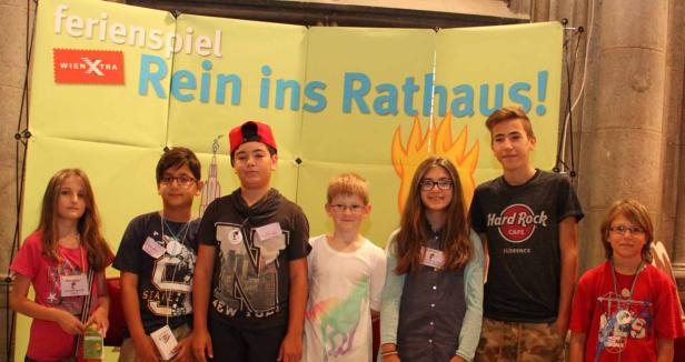 Eine Gruppe von Kindern steht vor einem Banner mit der Aufschrift „Rein ins Rathaus!“.