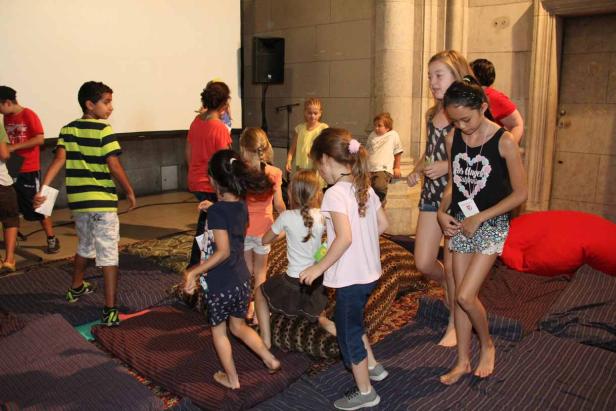 Eine Gruppe Kinder spielt und tanzt in einem Raum mit Kissen und Matten.