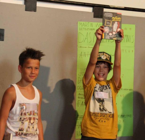 Ein Junge hält das Buch „Das Mumiengemälde“ hoch, während ein anderer Junge daneben steht.