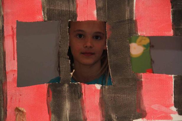 Ein junges Mädchen schaut durch eine bemalte Pappkonstruktion.