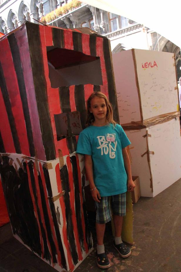 Ein junges Mädchen steht vor bemalten Pappkartons.
