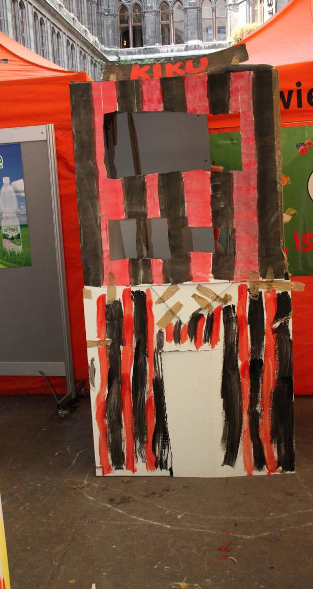 Ein bemalter Pappaufsteller mit dem Schriftzug „KiKu“ steht im Freien.