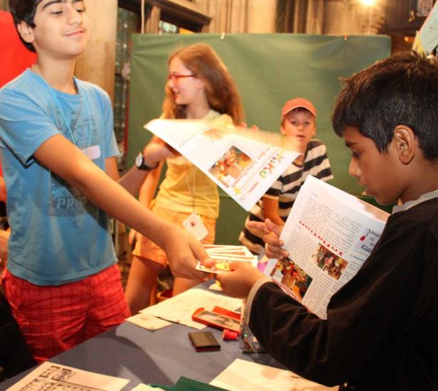 Eine Gruppe Kinder steht an einem Tisch und liest oder verteilt Flyer.
