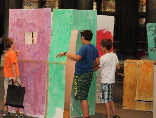 Drei Jungen betrachten und berühren eine bemalte Installation aus Karton.