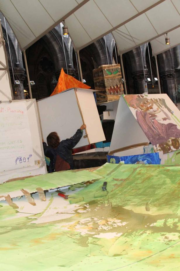 Eine Person arbeitet an einem Kunstprojekt mit bemalten Häusern in einem Innenraum.