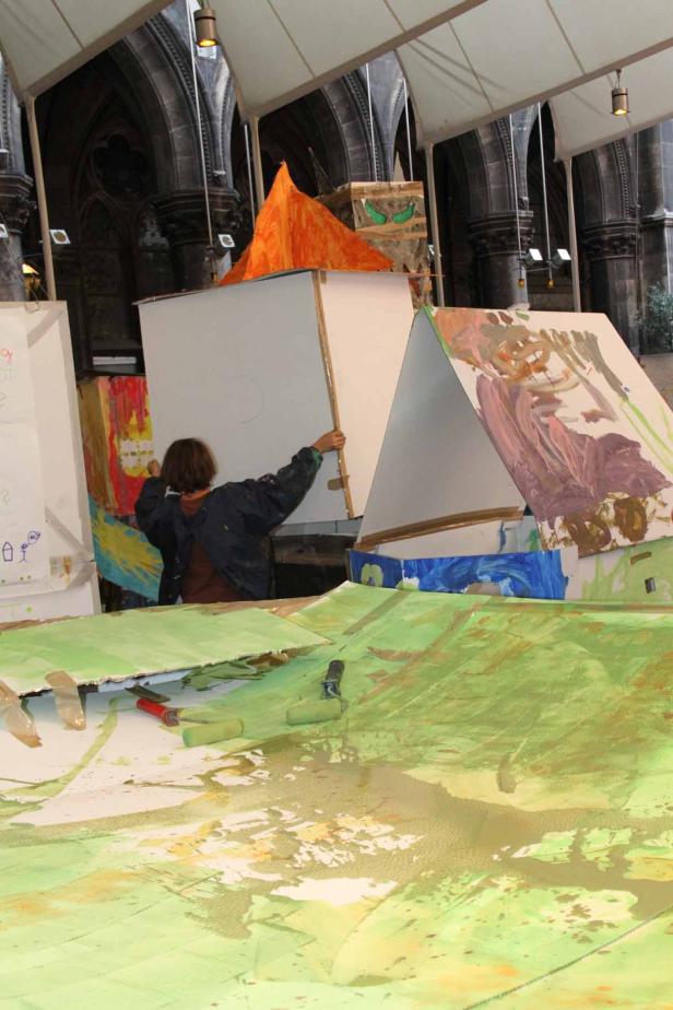 Eine Person arbeitet an einer Installation mit Farbe und Karton in einem Raum mit hohen Decken.