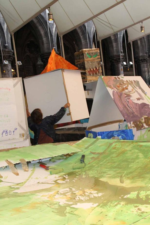 Eine Person arbeitet an einem Kunstprojekt mit bemalten Kartons in einem Innenraum.