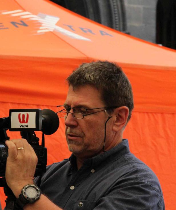 Ein Kameramann von W24 filmt vor einem orangefarbenen Hintergrund.