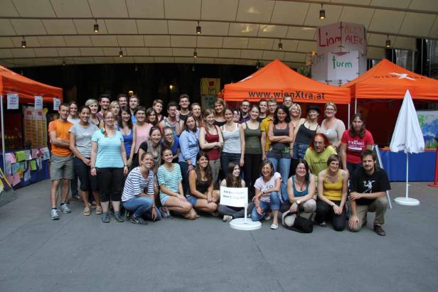 Eine Gruppe von Menschen posiert vor orangefarbenen Zelten von WienXtra.