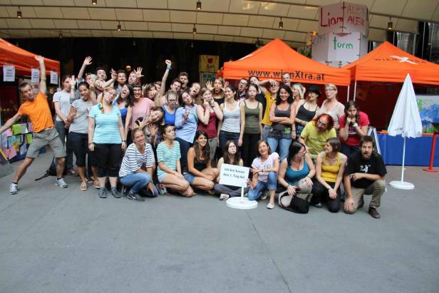 Eine große Gruppe von Menschen posiert vor orangefarbenen Zelten für ein Foto.