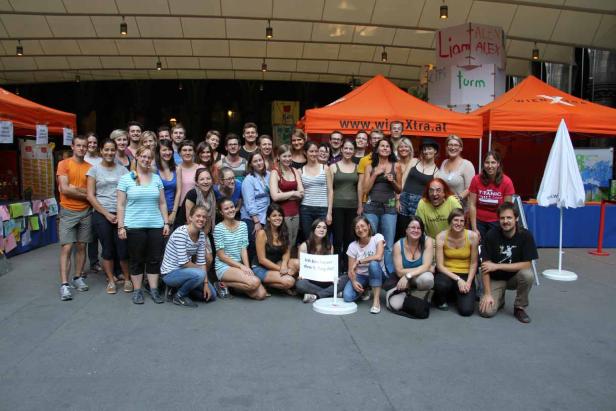 Eine große Gruppe von Menschen posiert vor orangefarbenen Zelten für ein Foto.