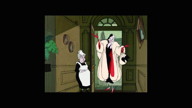 Cruella de Vil steht mit einer Haushälterin in einem Flur.