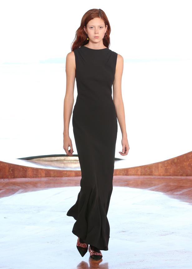 Eine Frau präsentiert ein ärmelloses, schwarzes Abendkleid auf einem Laufsteg.