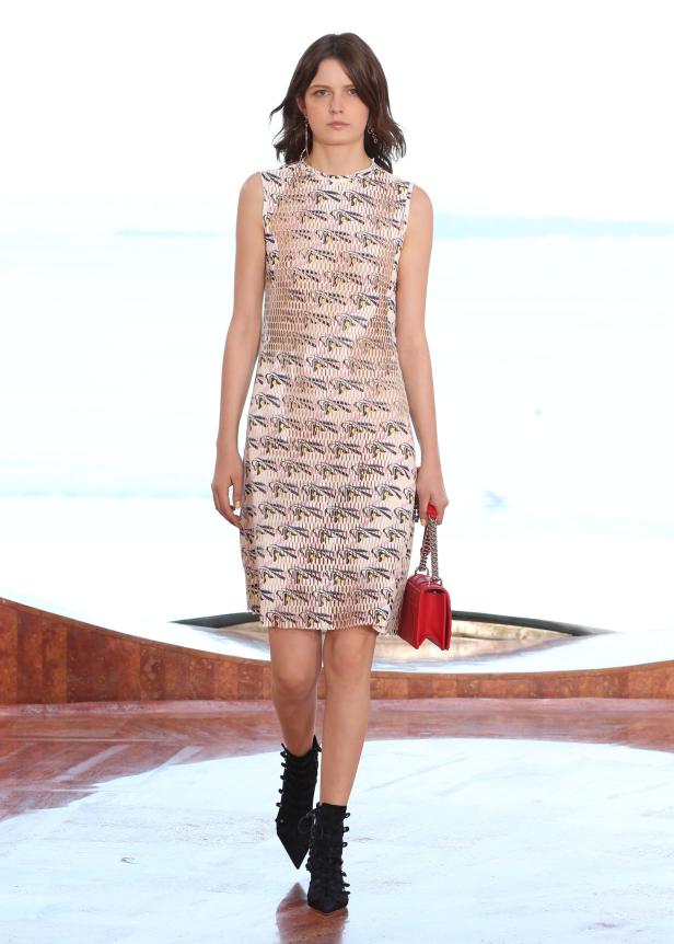 Eine Frau in einem gemusterten Kleid und schwarzen Stiefeln mit einer roten Handtasche.