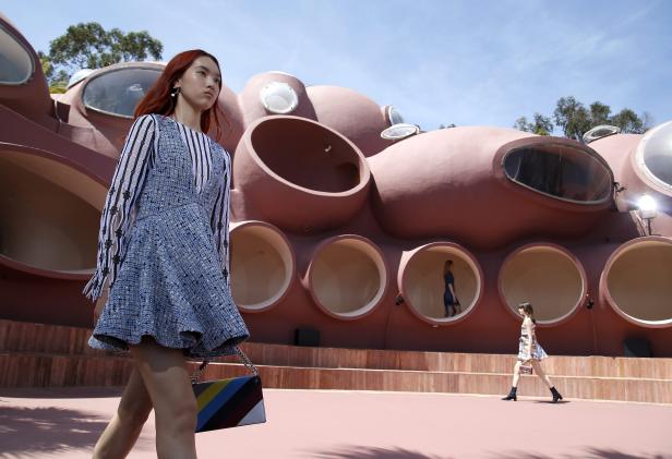 Eine Frau läuft auf einem Laufsteg vor einem ungewöhnlichen, kuppelförmigen Gebäude.