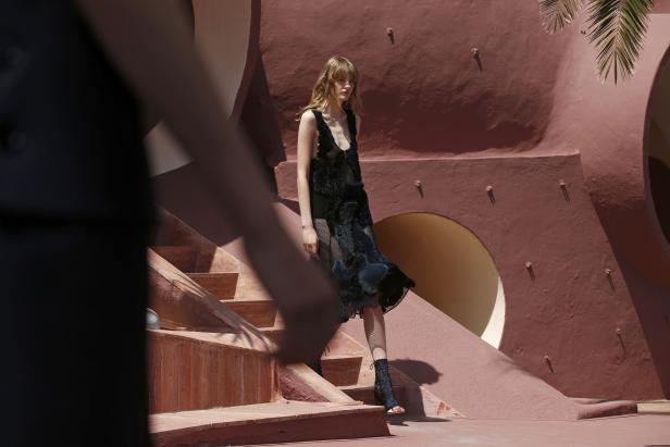 Eine Frau in einem Kleid steht auf einer Treppe vor einem rosafarbenen Gebäude.