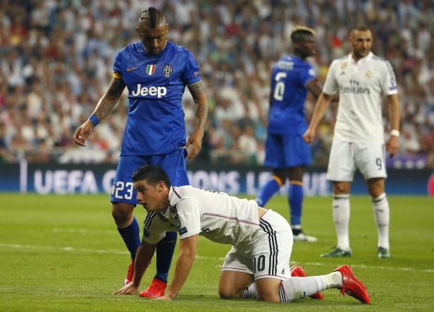 Ein Fußballspieler kniet auf dem Rasen, während andere Spieler im Hintergrund stehen.