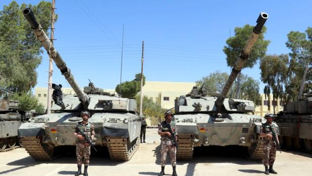 Soldaten stehen vor zwei Panzern mit erhobenen Geschützen.