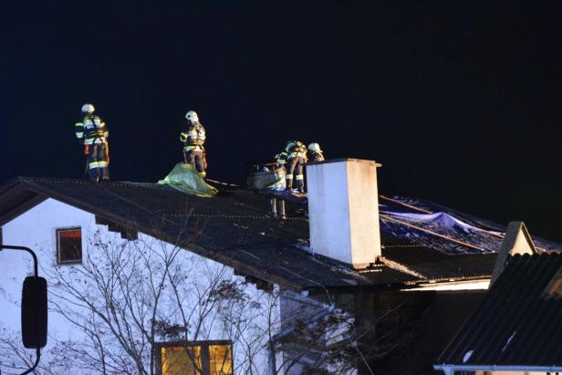 Mehrere Feuerwehrleute arbeiten nachts auf dem Dach eines Hauses.