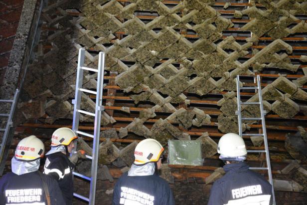 Feuerwehrleute begutachten ein beschädigtes Dach mit Leitern.