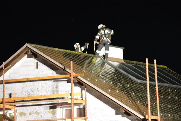 Zwei Feuerwehrleute arbeiten nachts auf dem Dach eines Hauses.