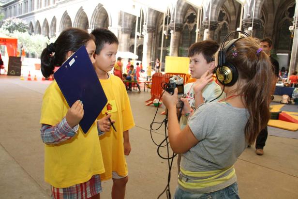 Kinder interviewen sich gegenseitig mit einem Aufnahmegerät und einem Klemmbrett.