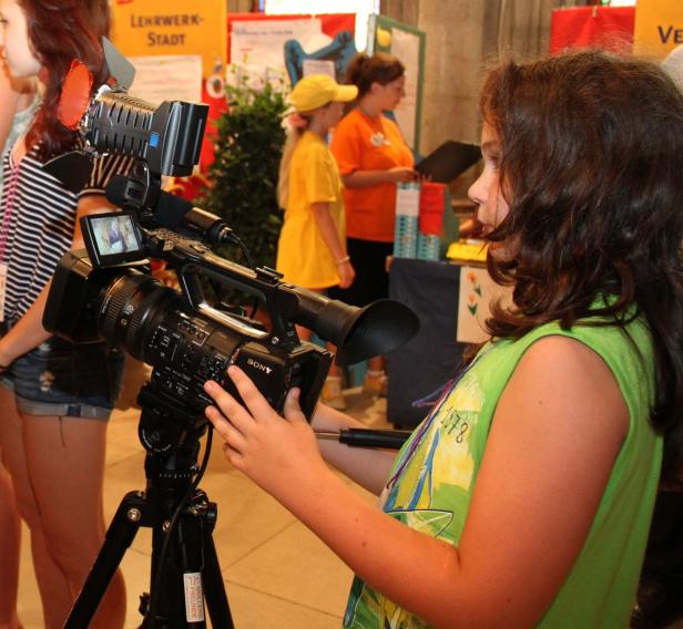 Ein junges Mädchen bedient eine professionelle Videokamera auf einem Stativ.