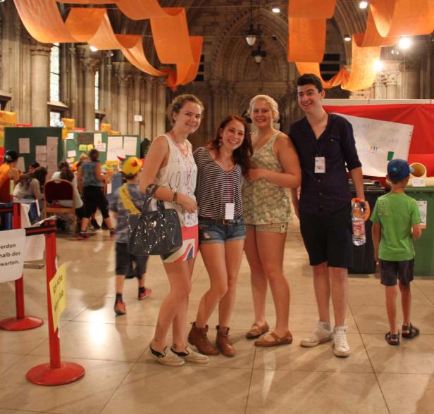 Eine Gruppe junger Leute posiert in einer Halle mit orangefarbenen Dekorationen für ein Foto.