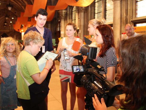 Eine Gruppe von Jugendlichen filmt eine Szene in einem großen Raum mit orangefarbenen Dekorationen.