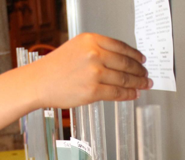 Eine Hand ordnet ein Blatt Papier an einer Reihe von beschrifteten Röhrchen.