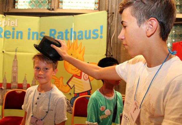 Ein Junge setzt einem anderen Jungen einen schwarzen Zylinder auf den Kopf.