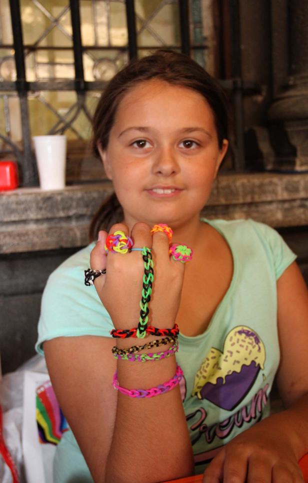 Ein Mädchen präsentiert selbstgemachte Armbänder und Ringe aus Gummibändern.