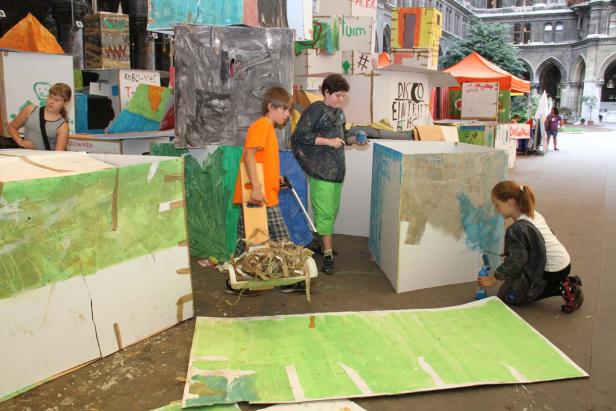 Kinder bemalen Pappkartons mit Farbe in einem Innenhof.