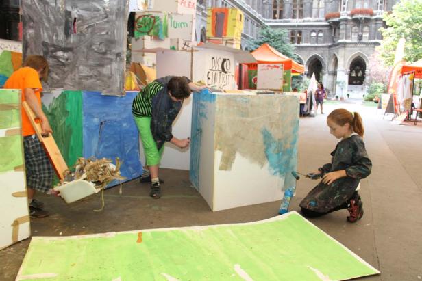 Kinder bemalen Pappkulissen mit Farbe im Freien.
